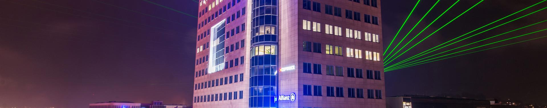 Das erste Hochhaus Deutschlands steht noch heute mitten in Jena, bei Nacht, mit grünen Lasern