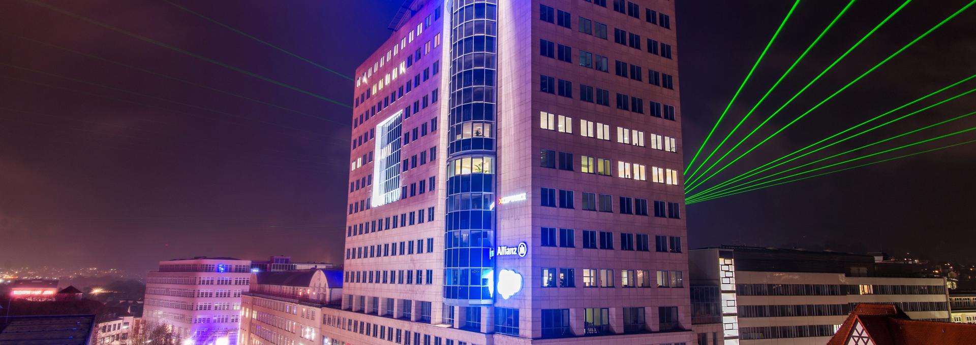 Das erste Hochhaus Deutschlands steht noch heute mitten in Jena, bei Nacht, mit grünen Lasern