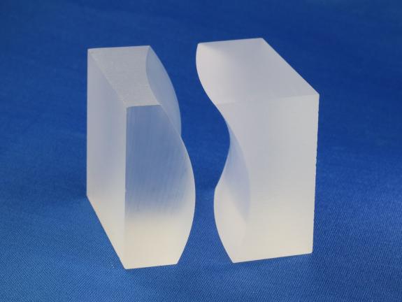 Vor einem blauen Hintergrund stehen zwei weiße Glasstücke mit unterschiedlichen Formen. Sie passen ineinander.