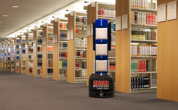 Ein mobiler Serviceroboter steht in einer Bibliothek vor Buchreihen.