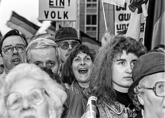 Das schwarz-weiß-Foto zeigt einen Ausschnitt einer Menschenmenge, die interessiert nach vorn schauen. Im Mittelpunkt eine Frau, die jubelt.