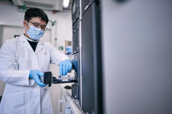Ein Mann im Laborkittel stellt kleine Ampullen in ein Analysegerät