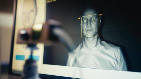 Auf dem Bild ist eine Person zu sehen, die in ein Kamerasystem blickt. Auf einem Monitor wird das Gesicht der Person gezeigt. Dabei erkennt der Sensor die Augen des Betrachters. Diese sind gekennzeichnet.