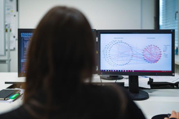 Eine Person vor einem Computerbildschirm, auf dem ein Netz zwischen den Namen verschiedener Mikroorganismen gesunder und kranker Probanden zu sehen ist