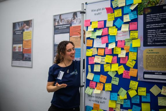 Dr. Mathilde Gallistl steht vor der „Ressourcen-Wand“, an der Besucher:innen anonym auf Zetteln notieren konnten, was ihnen Kraft gibt. Andere Besucher:innen können die Beiträge lesen und sich davon inspirieren lassen.