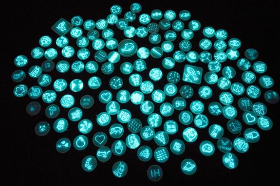 Fluoreszierende Mikroben in Petrischalen, die verschiedene Motive abbilden.