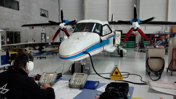 Kleines Forschungsflugzeug steht in einer Werkhalle neben technischen Geräten und Ausrüstung.