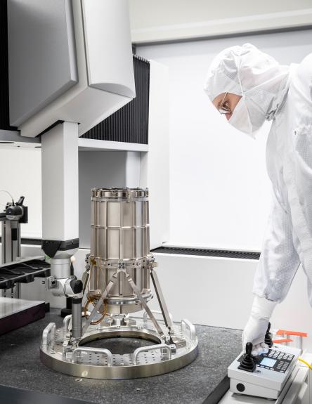   Person in weißem Schutzanzug bedient ein metallisches Testsystem in einem Labor.